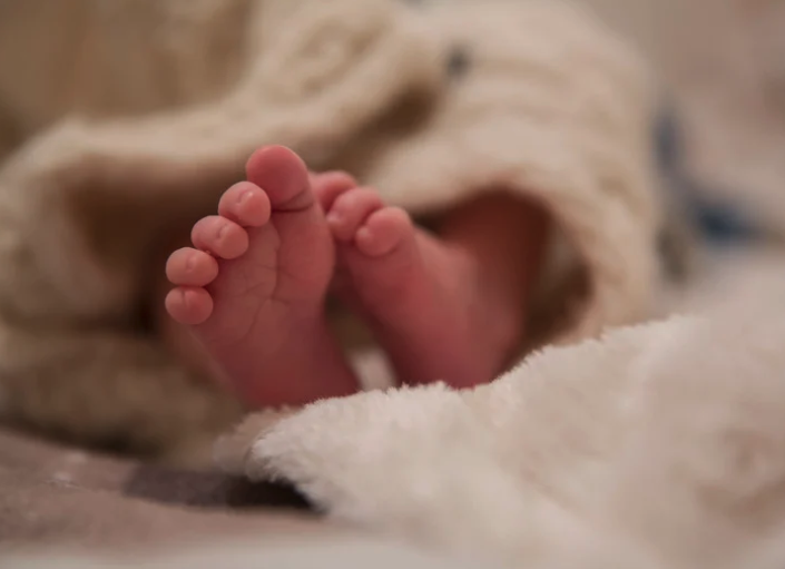 Babyfüße in den Händen der Mutter neben einer feinen Goldkette